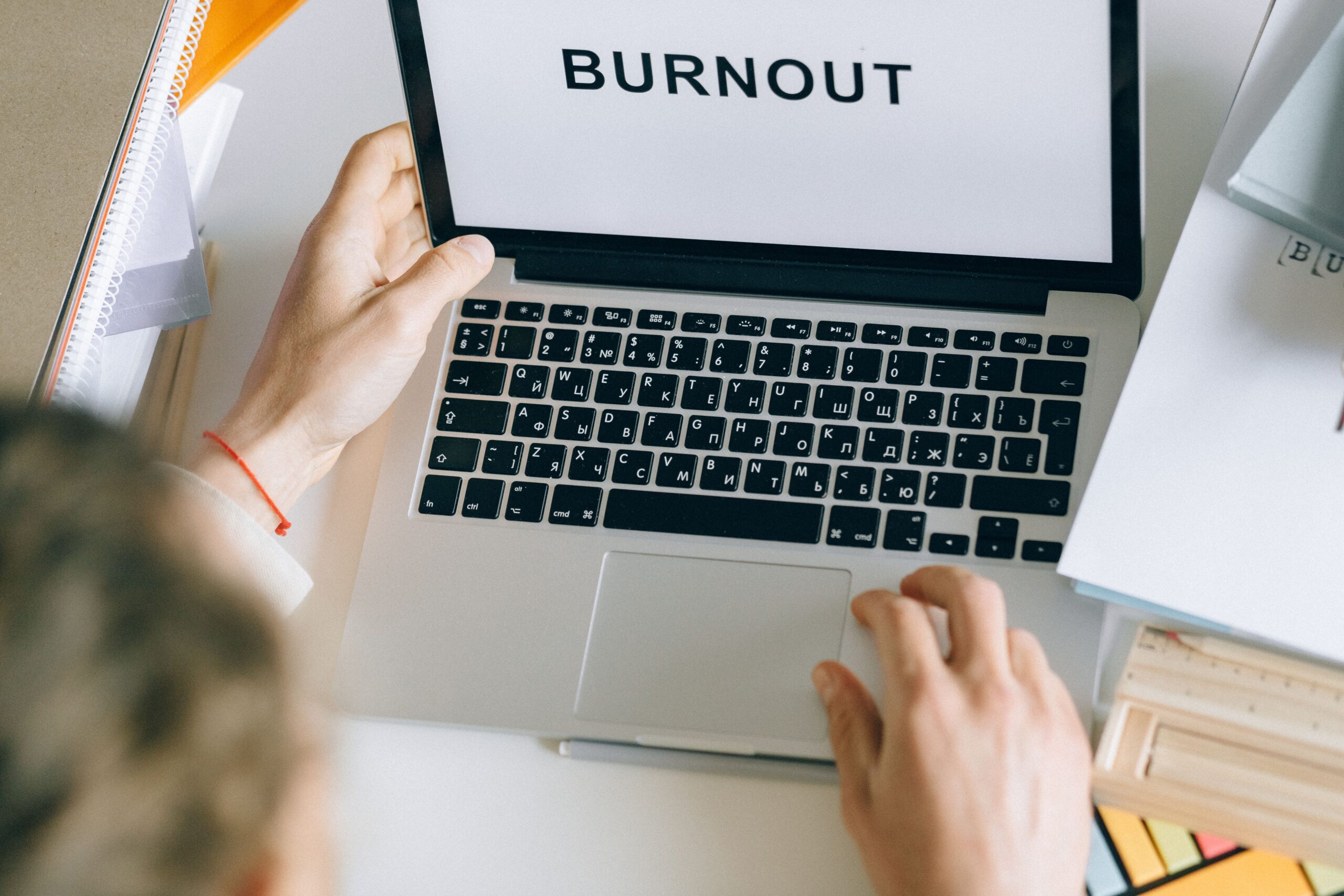 Overhead view of a person typing 'BURNOUT' on a laptop, surrounded by office materials.